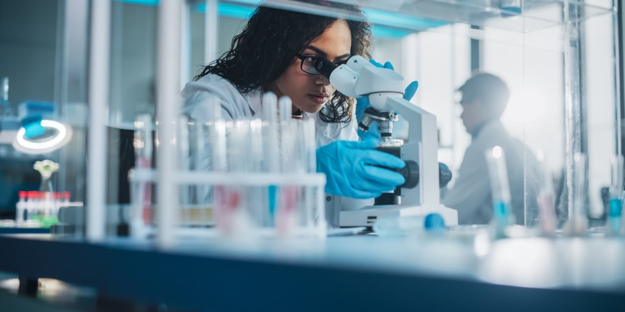 Medical professional looking into a microscope in a lab setting.