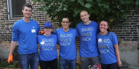 A group of Baird Capital associates standing arm in arm wearing Baird Gives Back t-shirts.