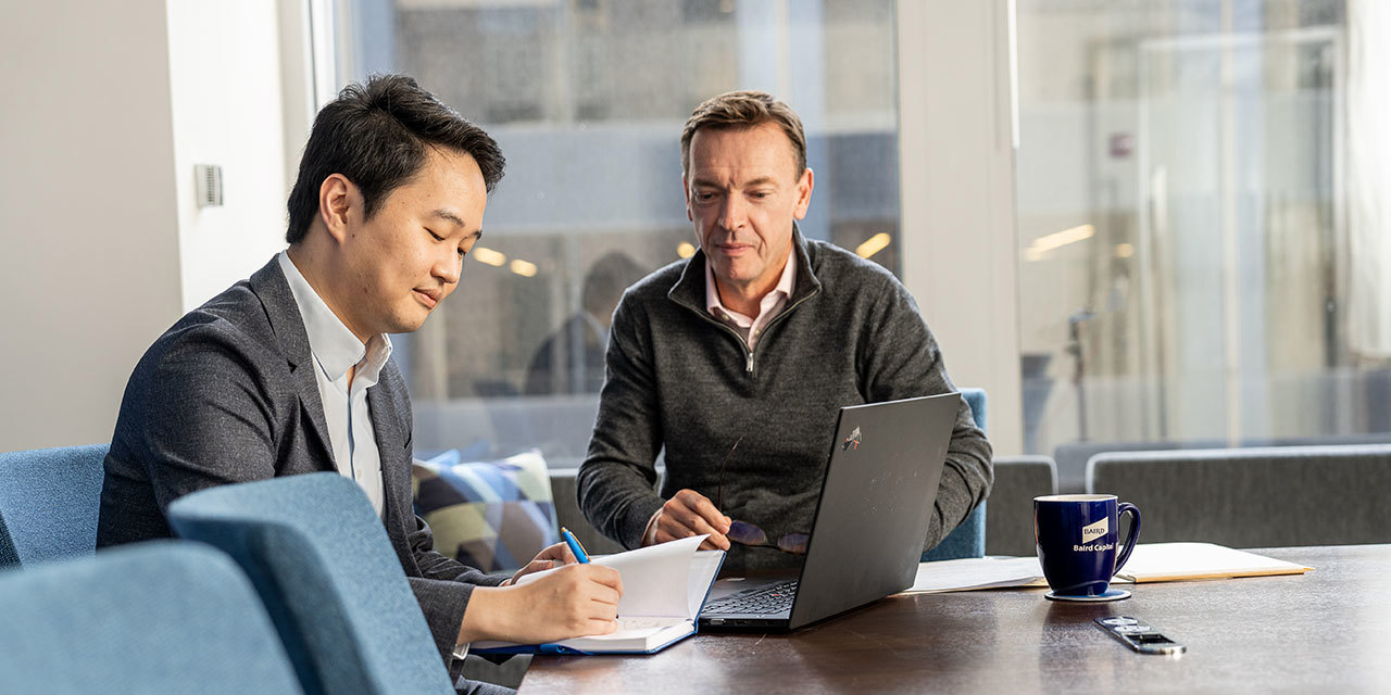 Two Baird Capital associates meeting at a conference room table looking at a laptop