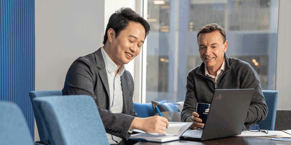 Two associates meeting on a conference room. One person writing in a notebook and using a laptop