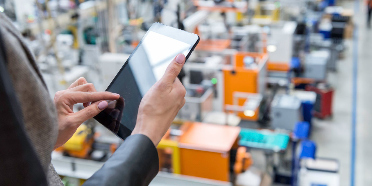 Hands holding an iPad overlooking a manufacturing floor